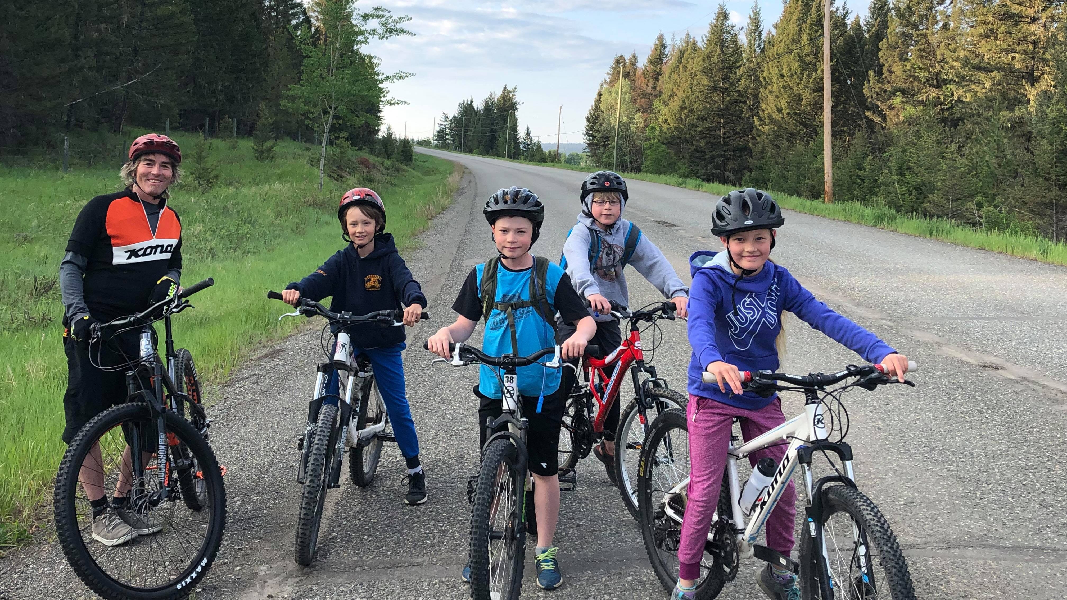 Four children and an adult smile at the camera on their bikes with helmets.